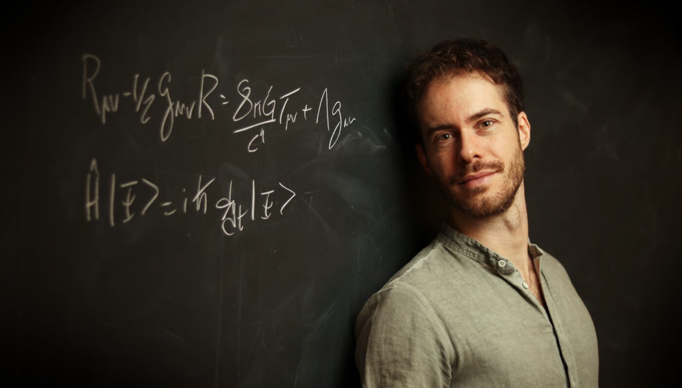 Guilherme Franzmann standing beside a blackboard covered with equations