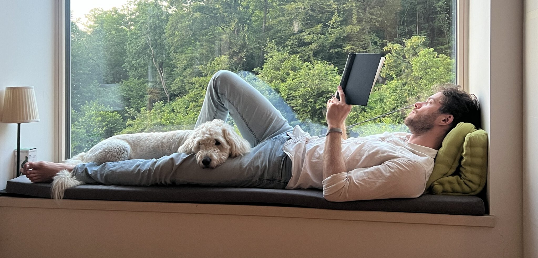 Guilherme Franzmann reading beside a dog on a window seat