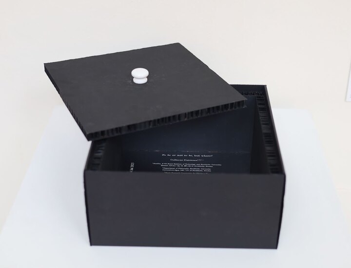 An open black box containing a printed scientific paper on a reflective interior, with its removable lid resting above.