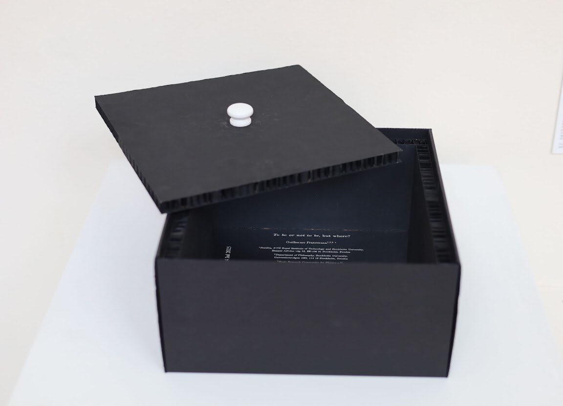 An open black box containing a printed scientific paper on a reflective interior, with its removable lid resting above.
