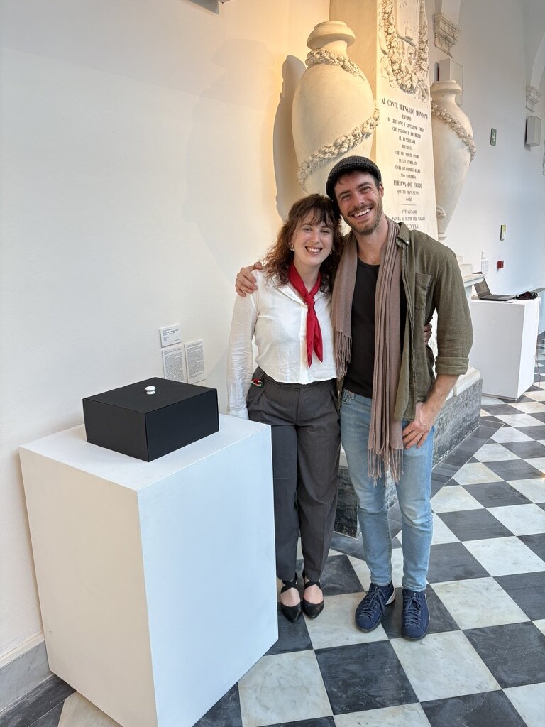 Jennifer Taufer and Guilherme Franzmann standing beside the artwork at mudaC in Carrara.